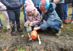 Dwoje dzieci podlewa sadzonki wodą z konewki.