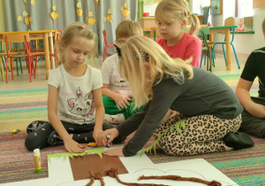 Dwie dziewczynki przyklejają szablon trawy na wspólną pracę plastyczną pt. "Nasze drzewo z dobro-sadu".