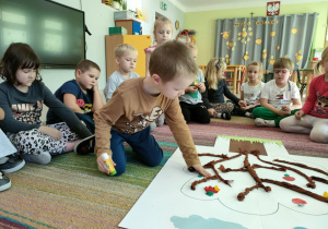 Chłopiec przykleja szablon jabłka na wspólną pracę plastyczną pt. "Nasze drzewo z dobro-sadu".