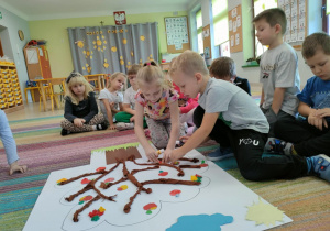 Dwoje dzieci przykleja szablon jabłka na wspólną pracę plastyczną pt. "Nasze drzewo z dobro-sadu".