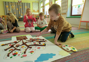 Chłopiec odbija palce umoczone w farbach w kolorach jesieni, tworząc jesienne liście na naszej jabłoni.