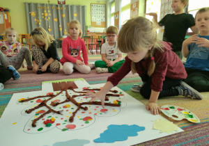 Dziewczynka odbija palce umoczone w farbach w kolorach jesieni, tworząc jesienne liście na naszej jabłoni.