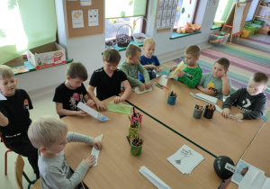 Chłopcy składają samolot wg instrukcji słownych nauczycielki.