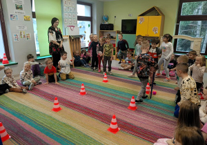 Dwie drużyny rywalizują między sobą. Prowadzą piłkę między pachołkami. Reszta dzieci dopinguje swoich kolegów i koleżanki.