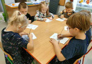 Kilkoro dzieci przy stole rozwiązuje kartę pracy "Zdrowe słodkości".