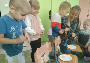 Maluszki nawijają sznurek na rolkę prezentując misia wciągającego spaghetti.