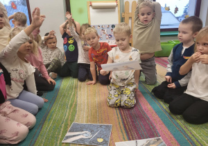 Dzieci siedzą w kole na dywanie. Wybrane dziecko opisuje, co znajduje się na obrazku.