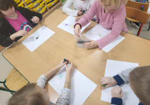 Kilkoro dzieci przy stole podczas tworzenia pracy plastycznej "Ukryte skarby".