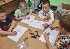 Kilkoro dzieci przy stole podczas tworzenia pracy plastycznej "Ukryte skarby".