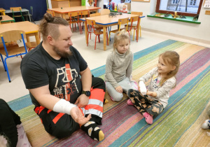 Pan Tomasz wraz z dziewczynką mają zabandażowaną rękę.