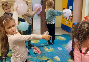 Czworo dzieci trzyma balon w dwóch dłoniach i wykonują skręt tułowia w prawo podczas zabawy ruchowej.