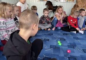 Dzieci z grupy "Biedronki" siedząc w kole na dywanie obserwują kostki, których wylosowana liczba oczek wskaże, jakie będzie kolejne wylosowane przedświąteczne zadanie.