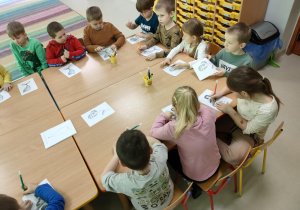 Dzieci siedzą przy połączonych stołach słuchając bajki, jednocześnie rysując kółko na ogonie, gdy usłyszały imię syrenki - Arielka.