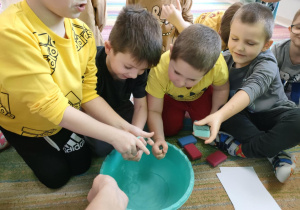 Młodsi chłopcy uczestniczą w mokrych zabawach z wodą i wyciskają gąbki.