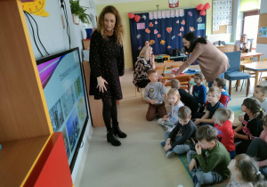 Dzieci siedzą na dywanie i rozwiązują zagadki, zaprezentowane przez p. Adę.