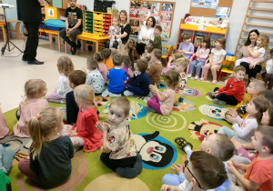 Dzieci siedzą na dywanie i śpiewają poznaną wcześniej piosenkę na powitanie.