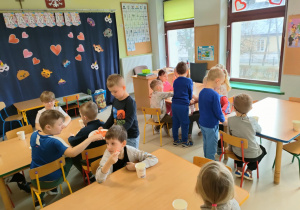 Dzieci z grupy "Pszczółek" siedzą przy stolikach i częstują się ekologicznymi owocami i warzywami oraz czystą, naturalną wodą.