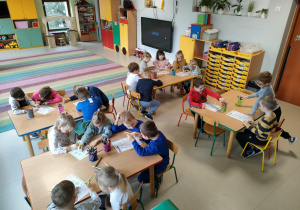 Dzieci z grupy "Pszczółek" przy stolikach pracują w parach i kolorują szablon piramidy zdrowego żywienia.