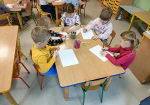 Kilkoro dzieci przy stoliku tworzy niespodziankę w formie ryrunku dla wybranej przez siebie, bliskiej osoby.
