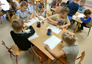 Kilkoro dzieci przy stoliku tworzy niespodziankę w formie ryrunku dla wybranej przez siebie, bliskiej osoby.