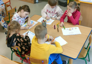 Kilkoro dzieci przy stoliku tworzy niespodziankę w formie ryrunku dla wybranej przez siebie, bliskiej osoby.