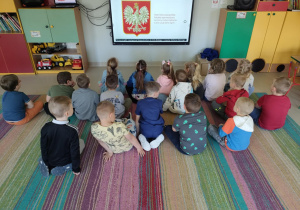 "Pszczółki" oglądają film edukacyjny nt. symboli narodowych na ekranie multimedialnym.