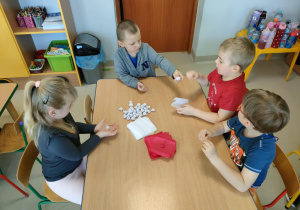 Kilkoro dzieci przy stoliku formuje kulki z bibuły.