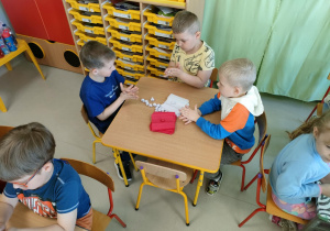 Kilkoro dzieci przy stoliku formuje kulki z bibuły.