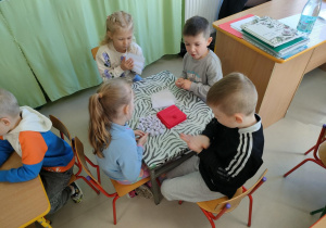 Kilkoro dzieci przy stoliku formuje kulki z bibuły.