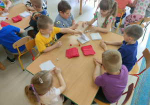 Kilkoro dzieci przy stoliku formuje kulki z bibuły.