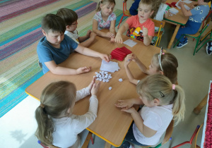 Kilkoro dzieci przy stoliku formuje kulki z bibuły.