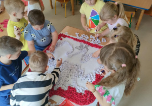 Część dzieci z grupy "Pszczółek" przykleja uformowane kulki z bibuły na szablon godła Polski.