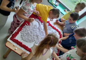 Część dzieci z grupy "Pszczółek" przykleja uformowane kulki z bibuły na szablon godła Polski.