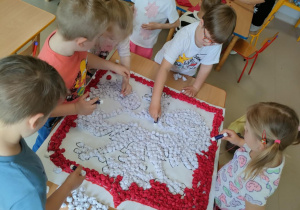 Część dzieci z grupy "Pszczółek" przykleja uformowane kulki z bibuły na szablon godła Polski.