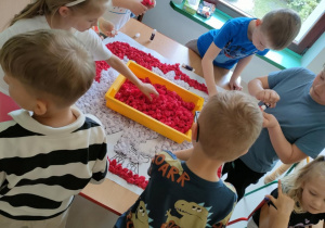 Część dzieci z grupy "Pszczółek" przykleja uformowane kulki z bibuły na szablon godła Polski.