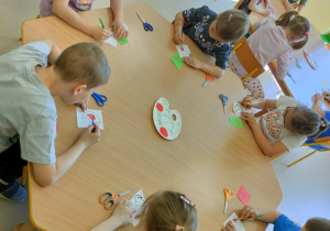 Kilkoro dzieci z grupy najstarszej przy stoliku maluje czerwoną farbą wybrane elementy na szablonie ptaka.