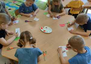 Kilkoro dzieci z grupy najstarszej przy stoliku maluje czerwoną farbą wybrane elementy na szablonie ptaka.