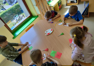 Kilkoro dzieci z grupy najstarszej przy stoliku maluje czerwoną farbą wybrane elementy na szablonie ptaka.