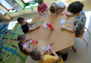 Kilkoro dzieci z grupy najstarszej przy stoliku maluje czerwoną farbą wybrane elementy na szablonie ptaka.