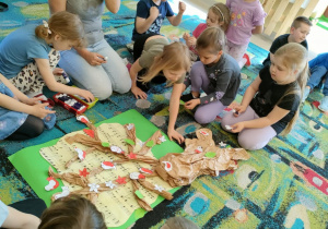Dzieci z grupy "Biedronek" po kolei przyklejają wycięte i pomalowane elementy na brystolu.