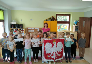 "Pszczółki" wraz z nauczycielką Justyną Skonieczka prezentują wykonaną przez siebie narodową dekorację, przedstawiającą godło Polski.
