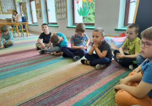 Dzieci siedzą na dywanie w kole i rozmawiają na temat treści usłyszanej bajki.