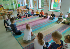 Dzieci siedzą w kole na dywanie i słuchają bajki pt. "Księżniczka na ziarenku grochu" w formie audiobooka.