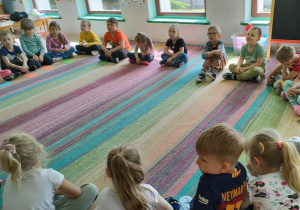 Dzieci siedzą w kole na dywanie i słuchają bajki pt. "Księżniczka na ziarenku grochu" w formie audiobooka.