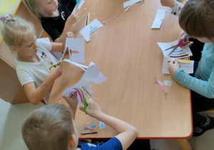 Dzieci przy trzecim stole wycinają elementy związane z treścią bajki.