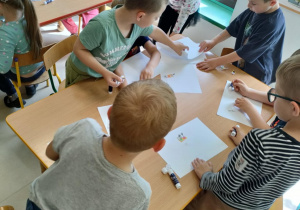 Kilkoro dzieci przy stole segreguje połączone obrazki kłódki i klucza wg kształtów.
