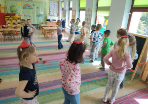 Dzieci maszerują po obwodzie koła z rękoma na bioderkach i woreczkiem na głowie. Starają się iść tak, by woreczek nie upadł na podłogę.