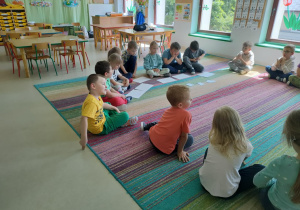 Dzieci siedzą w kole na dywanie i słuchają treści bajki w formie audiobooka.