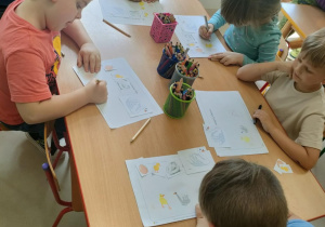 Dzieci siedzą przy stole i rysują cykl rozwojowy łabędzia.