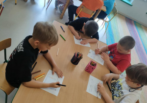 Kilkoro dzieci przy stole rysuje siebie i przyjaciół w zgodzie.